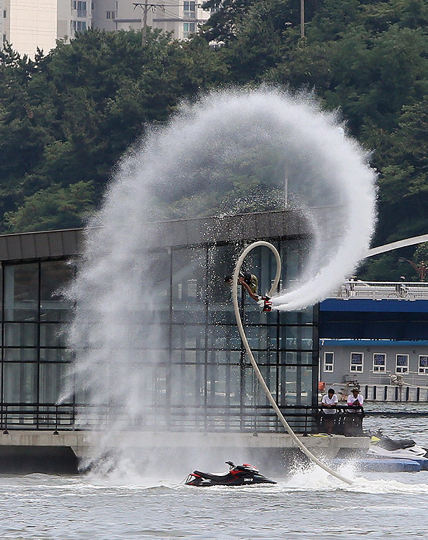 Състезател показва акробатични номера във въздуха с помощта на мощна струя вода, която го издига край пристанището на южнокорейския град Бусан