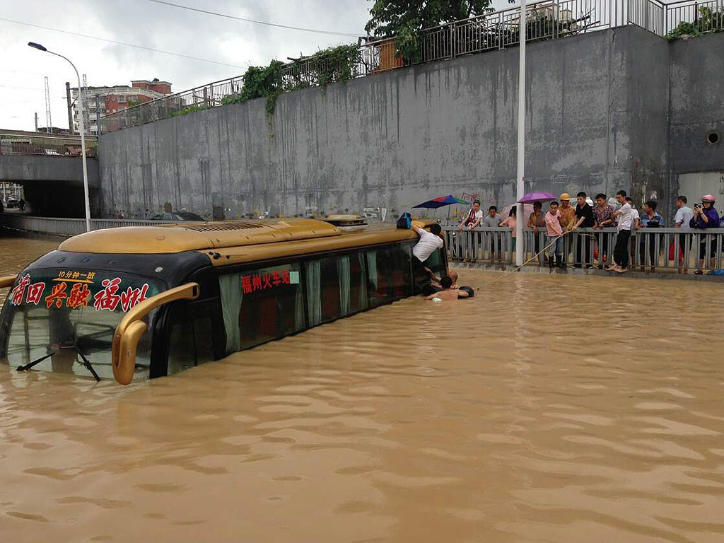 Хора евакуират пътници, блокирани в потопен автобус близо до железопътен мост в Фуджоу, в югоизточната част на Китай, провинция Фудзиен. Тайфуна Матмо е втория който удари Китай за една седмица, носейки с него проливни дъждове в провинцията.