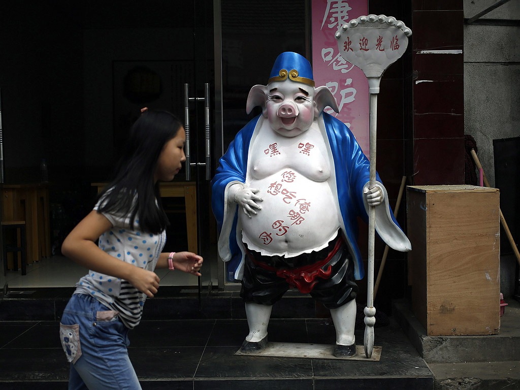 Китайка минава покрай скулптура на прасе пред ресторант в Пекин, Китай. На корема на прасето пише: "Кои части от мен желаете да ядете?" Китай отдавна е измъчван от различни скандали с безопасността на храните, включващи производителите на месо, мляко за бебета и дори бонбони от кисело мляко.