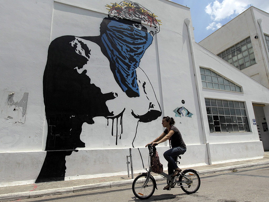 Жена се вози на велосипед покрай графит, изобразяващ статуята на Афродита с маска, в Атина, Гърция.