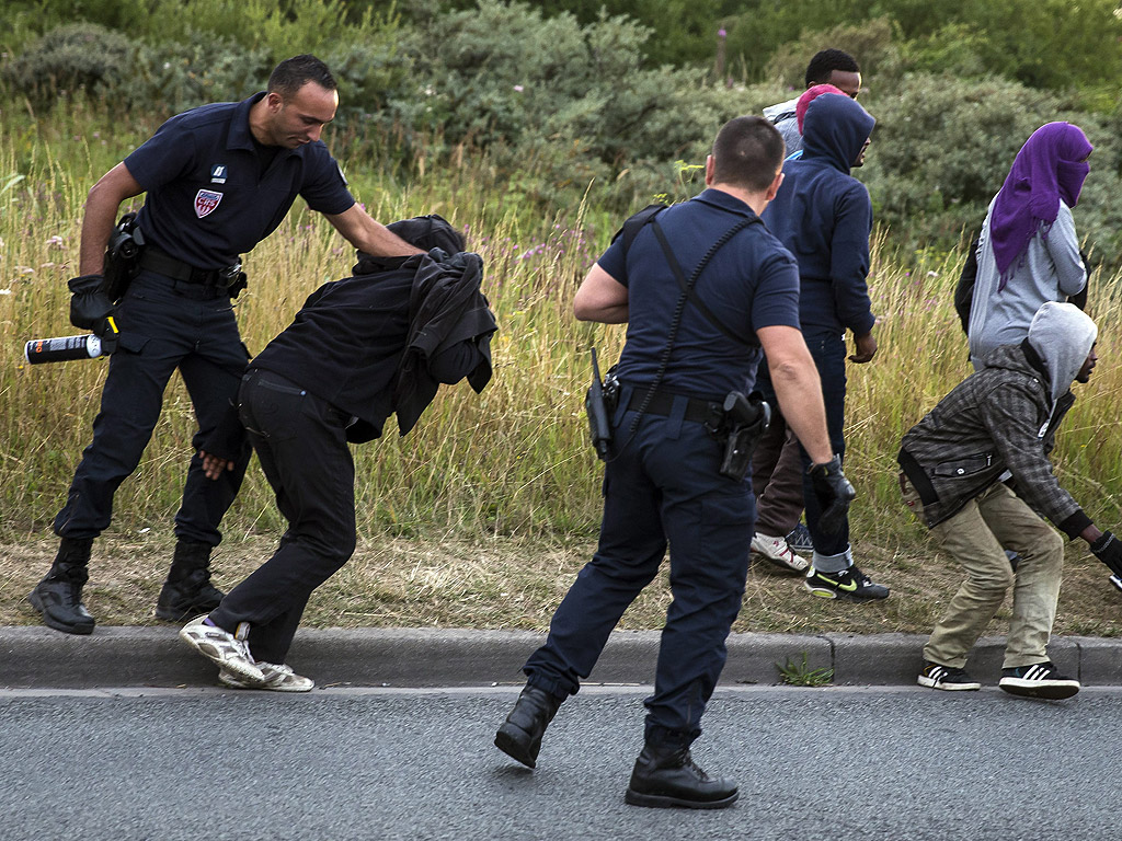 Френски полицаи ескортират мигранти от Еритрея, които чакат в близост до железопътните линии на Eurostar в покрайнините на Кале, Франция. Около 1700 опита за достъп до тунела под Ламанша, бяха направени от имигранти през цялата нощ на 2 август, да достигнат до Англия.