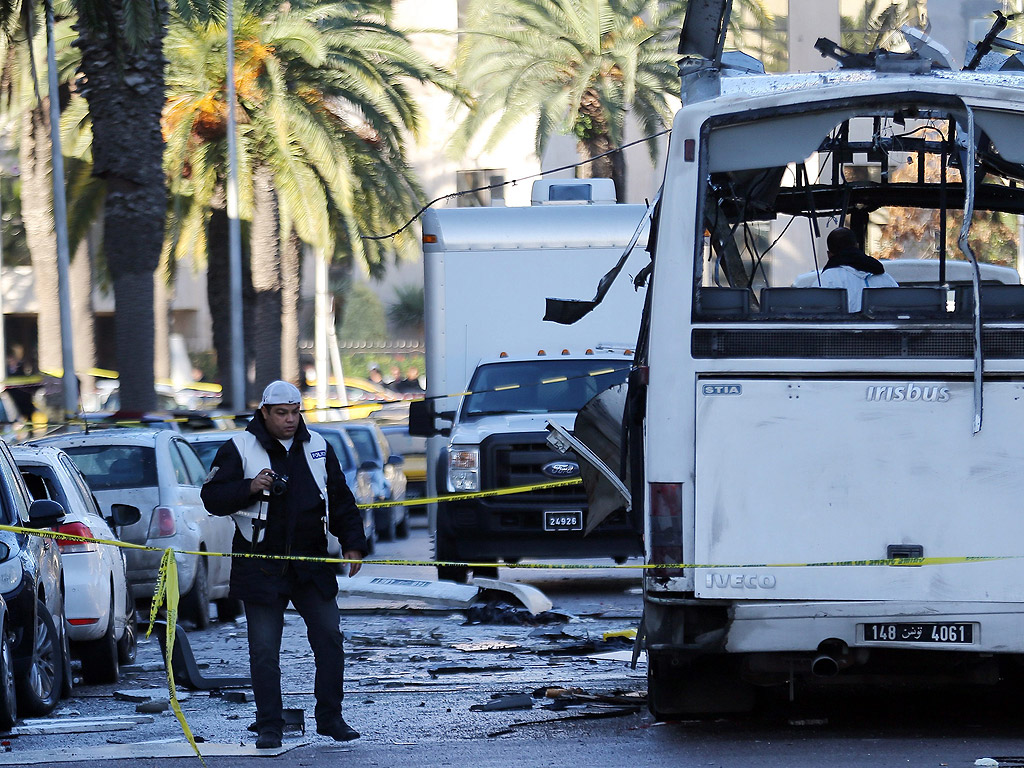 Тунизийски криминалисти проверяват останките на автобус превозващ президентската охрана в Тунис. Най малко тринадесет души са известни, че са били убити след бомбения взрив