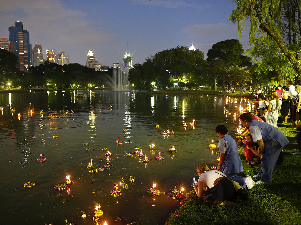 Хора край езеро в парка на годишния Лой Кратонг фестивал в Банкок, Тайланд. Фестивала на светлините, се провежда в съответствие с тайландския лунен календар при пълнолуние на дванадесетия месец и датира от повече от 700 години. Хората пускат по течението фенери в лотосови корита, съдържащи цветя, свещи и тамян по реките, езерата и океаните, с молитва да се разделят с лошия късмет на изминалата година и да отплава далеч от тях, така че техните нещастия да бъдат заменени с добра съдба през идващата година