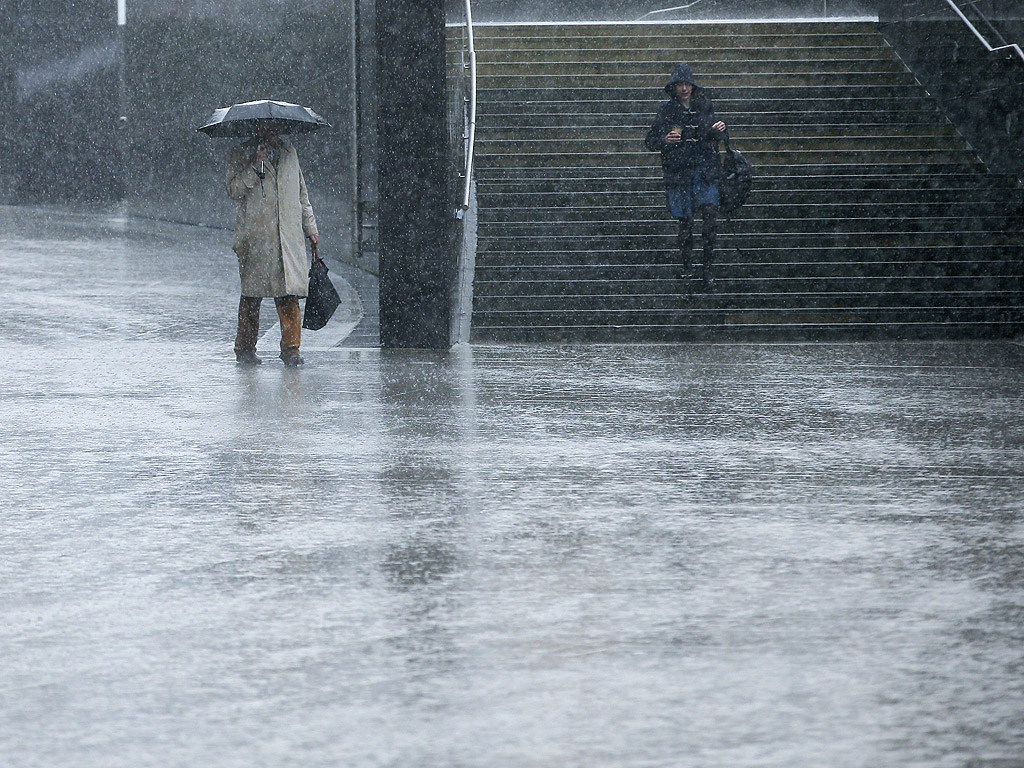 Хора се придвижват при силен вятър и дъжд по време на буря близо до централата на европейската комисия в Брюксел, Белгия