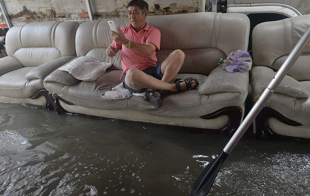 Мъж седнал на диван прави снимки на наводнението в Шенян, провинция Ляонин, североизточен Китай