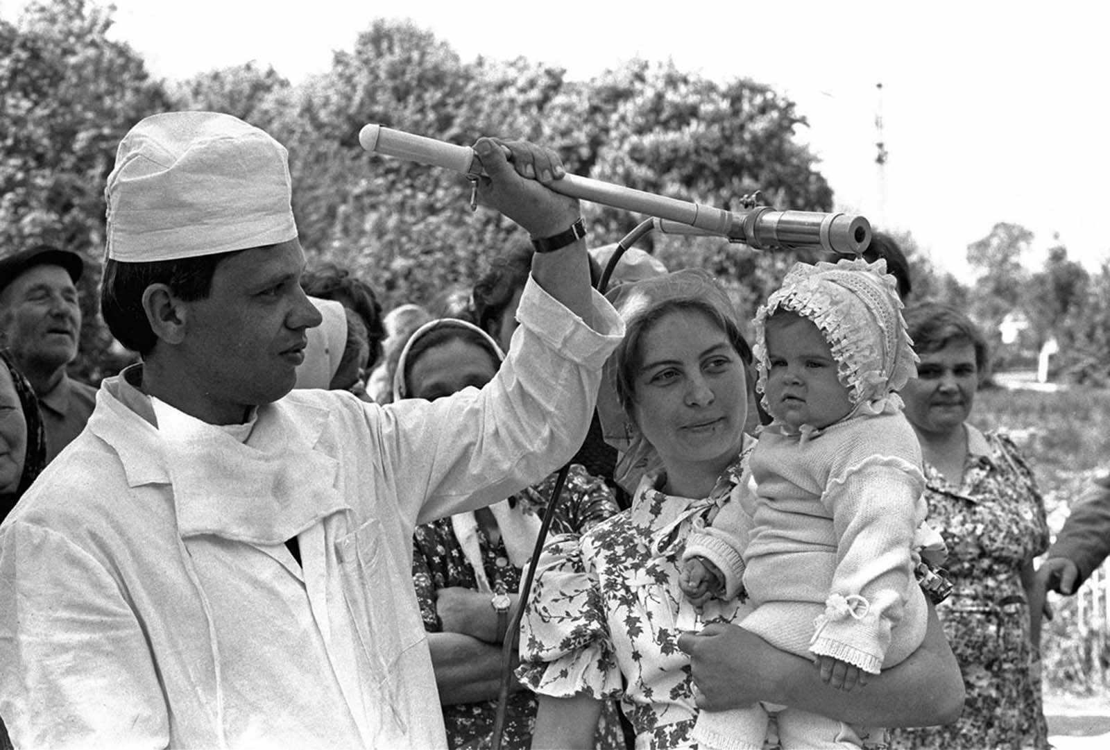 9 май 1986 г.: Съветски техник проверява бебе (Катя Литвинова) за радиокативно облъчване в село в близост да Киев.