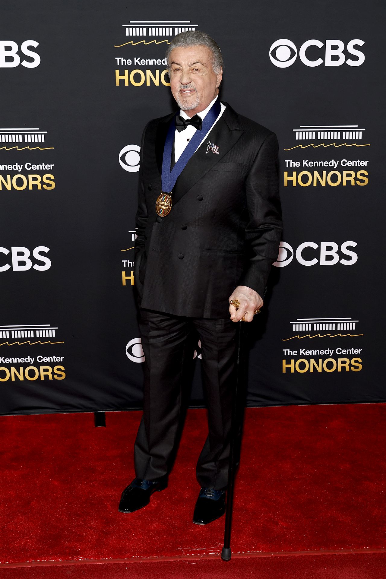 Легендата от „Роки“, на 79 години, се подпираше на елегантен черен бастун със златиста дръжка, докато правеше внушително влизане в Kennedy Center Opera House в събота вечер, където беше почетен като един от тазгодишните носители на отличието. ъпреки новата си опора на бастуна, Сталоун се усмихваше, разговаряше с други отличени и изглеждаше готов да се наслади на вечерта – макар че бавната и внимателна походка рязко контрастираше с безстрашния екшън герой.