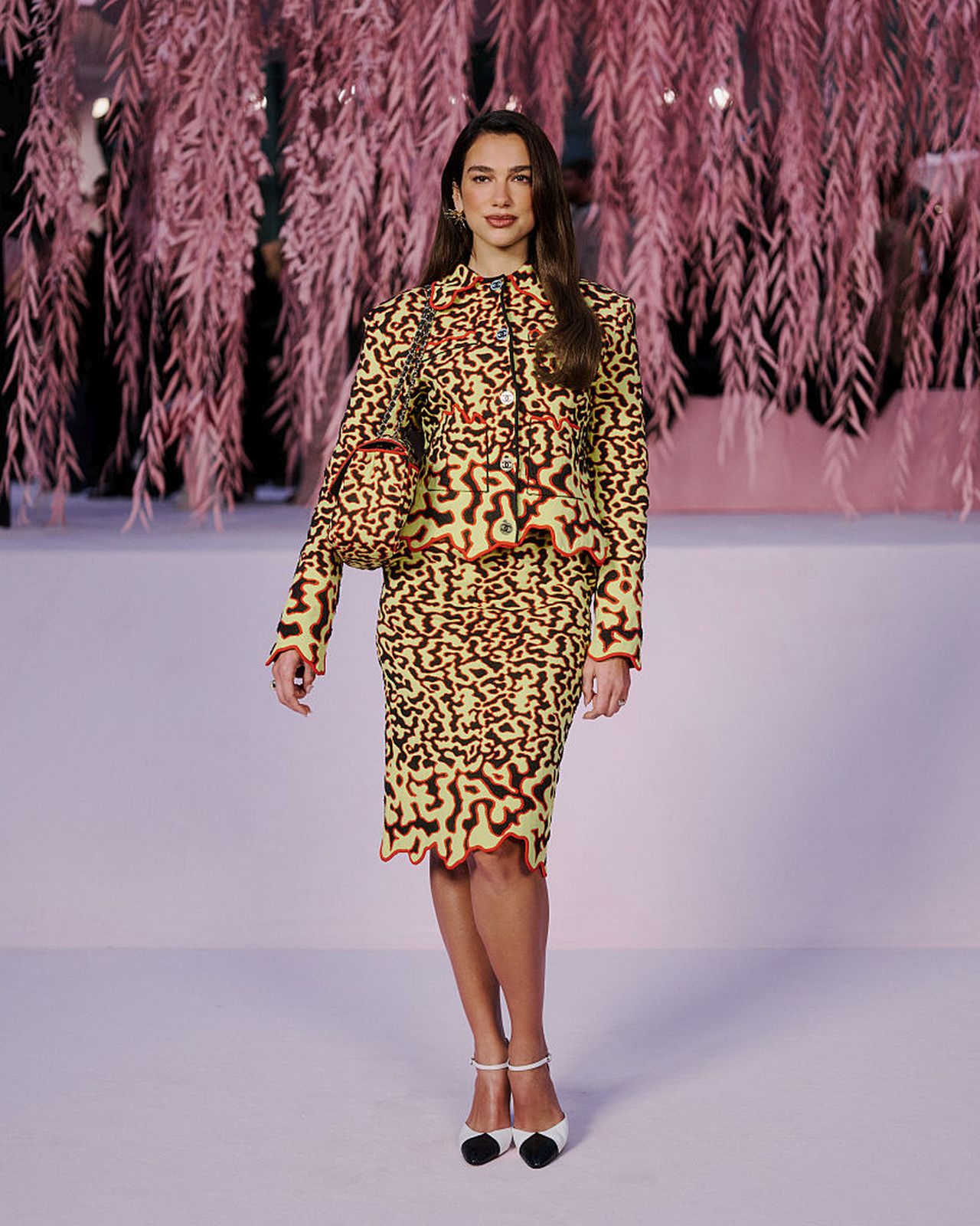 <p><strong>Дуа Липа</strong></p>

<p>Дуа Липа присъства на ревюто на Chanel по време на Haute Couture Week SS26, облечена в запомнящ се жълт комплект с пола и футуристичен &bdquo;разтопен&ldquo; принт в нюанси на оранжево, зелено и черно.</p>