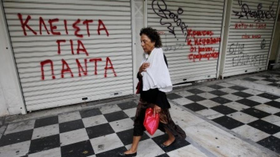 Жена минава покрай затворен магазин в центъра на Атина, на който е изписано 'Затворен завинаги'